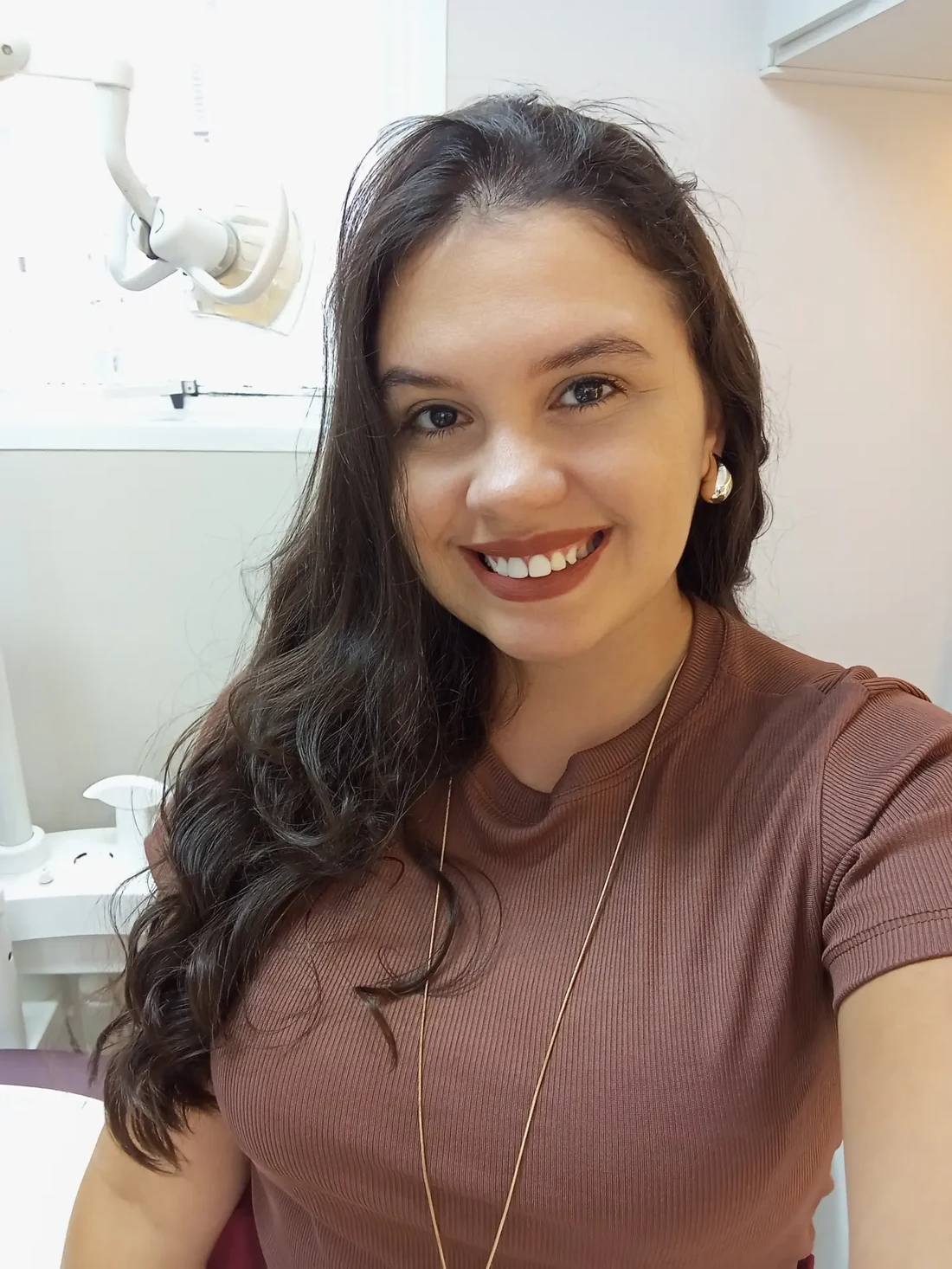 Dra. Jennifer Bianca sorrindo no consultório, com equipamento odontológico ao fundo